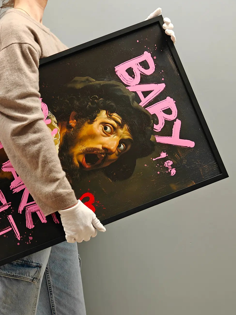 Person holding a framed art print with a stylized face and pink text on a gray background