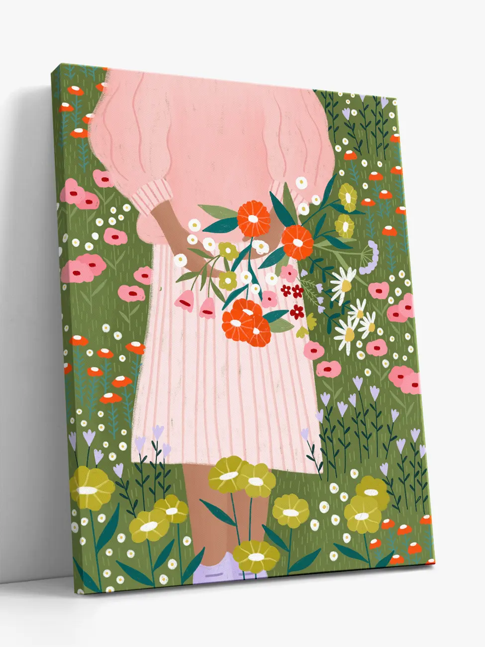A vertical canvas  print featuring a whimsical illustration of a woman in pink clothes holding a bouquet of orange and white flowers, set against a green field of wildflowers. The canvas is shown standing at an angle against a light gray wall.
