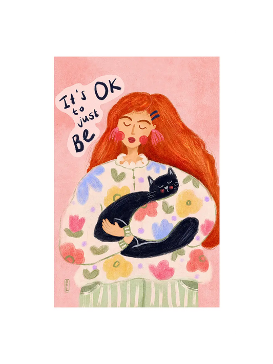 Art print of illustration in soft pink colors: woman holding a black cat with 'It's OK to just be' text on a pink background
