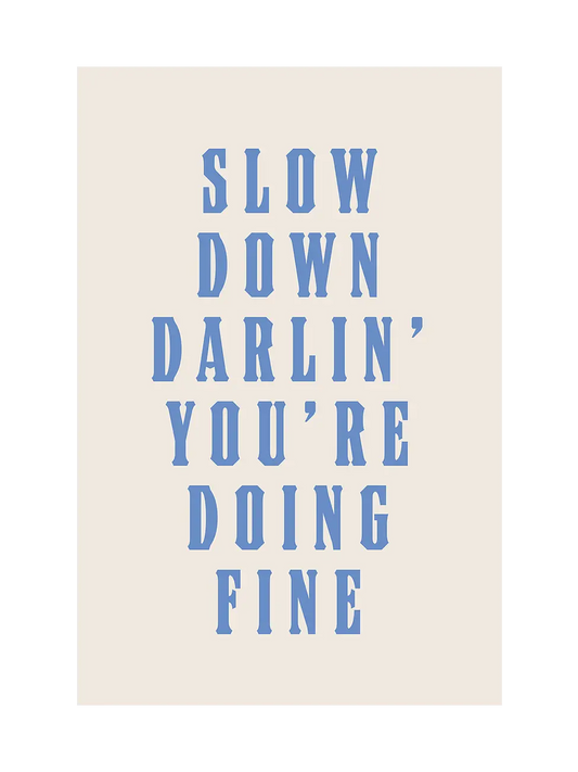 Типографски арт принт с надпис Slow Down Darlin’ You’re Doing Fine в светлосини букви върху топъл неутрален фон.